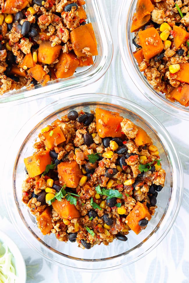 Ground chicken, sweet potato, black beans, corn garnished with coriander in meal prep containers.