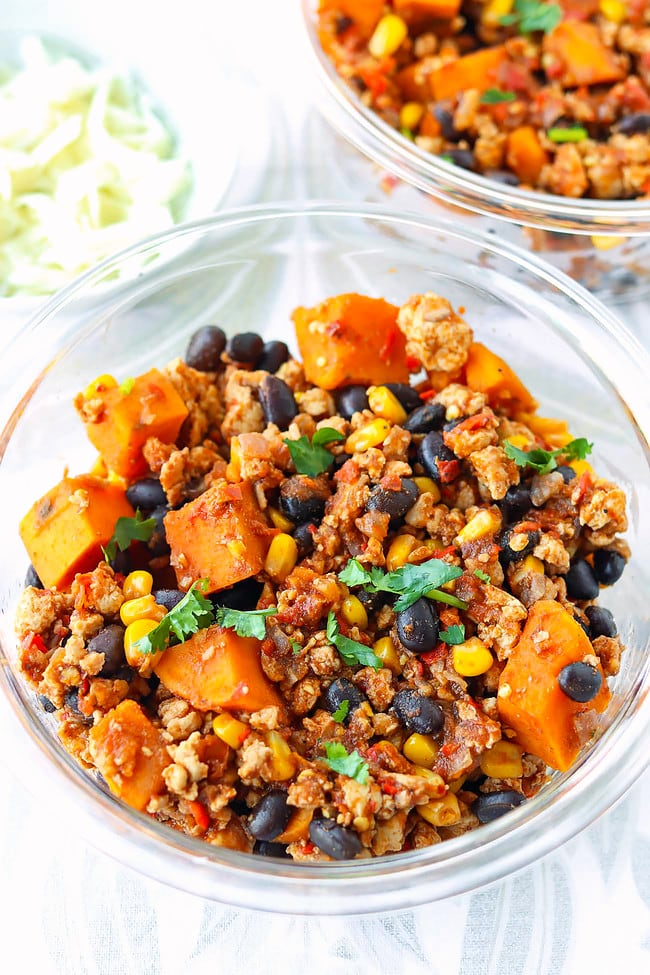 Closeup of Mexican ground chicken, sweet potato, black beans, corn garnished with coriander in containers.