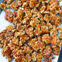 Granola clusters on a baking tray. Text overlay, "Peanut Butter Banana Protein Granola" and "thatspicychick.com".