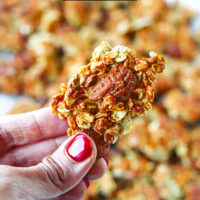 Hand holding up a granola cluster. Text overlay, "Peanut Butter Banana Protein Granola" and "thatspicychick.com".