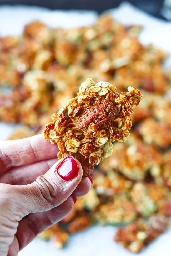 Hand holding up a peanut butter banana granola cluster above tray with granola clusters.