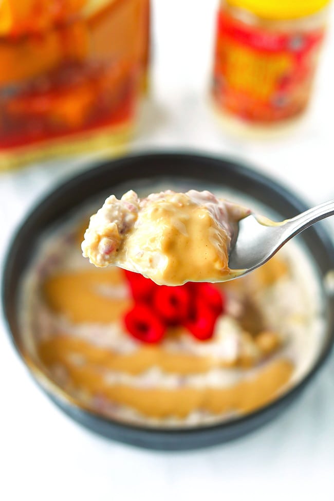 Spoon holding up a bite of salted caramel raspberry overnight oats with peanut butter drizzle.