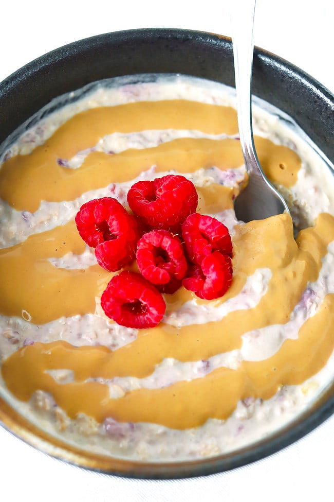 Spoon in bowl with salted caramel overnight oats and raspberries.