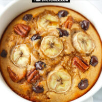 Closeup front view of baked oats in a ramekin with handles. Text overlay "Banana Bread Protein Baked Oats" and "thatspicychick.com".