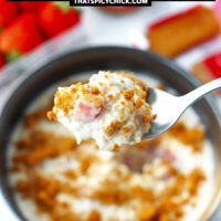 Spoon holding up a bite of overnight oats and crumbled Biscoff cookie. Text overlay "Biscoff Overnight Oats with Strawberries" and "thatspicychick.com".
