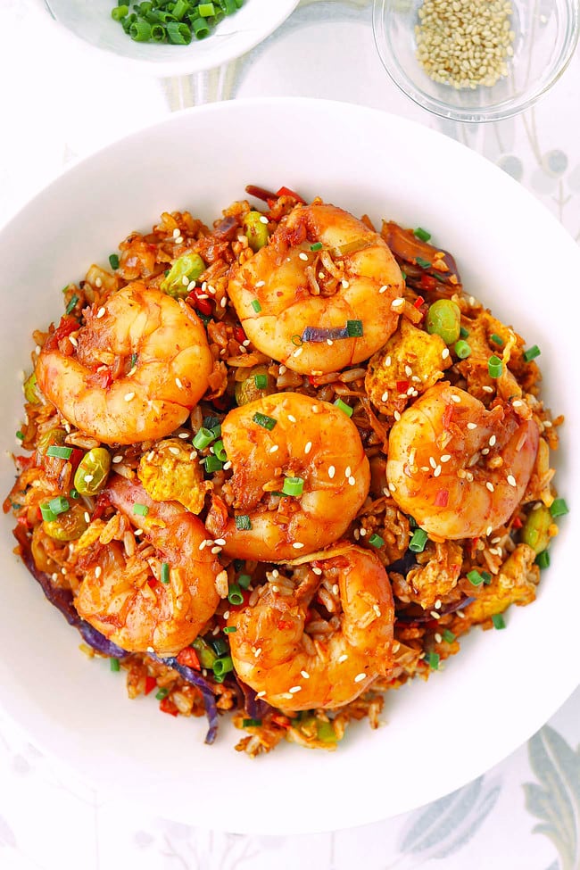 Korean fried rice with jumbo shrimp on a plate and garnishes in bowls behind.