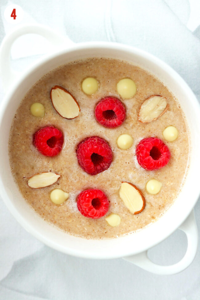 Raspberry white chocolate baked oats batter in ramekin with toppings.