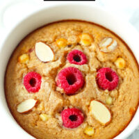 Closeup front view of raspberry baked oats in a ramekin. Text overlay "Raspberry White Chocolate Baked Oats" and "thatspicychick.com".