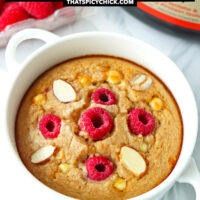 Ramekin with baked oats and protein powder and raspberries behind. Text overlay "Raspberry White Chocolate Baked Oats" and "thatspicychick.com".