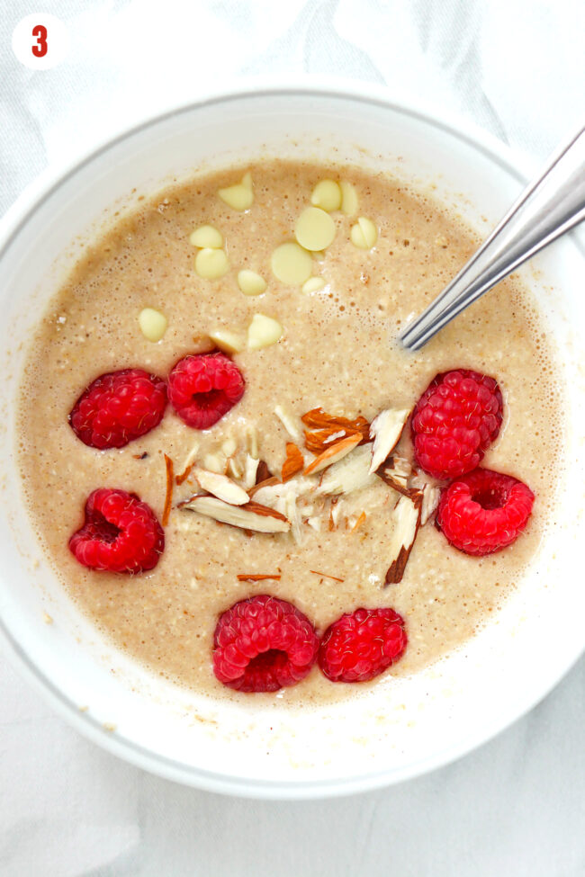 Batter for baked oats topped with raspberries, white chocolate chips and sliced almonds in a bowl