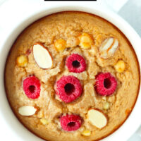 Overhead view of raspberry baked oatmeal in a ramekin. Text overlay "Raspberry White Chocolate Baked Oats" and "thatspicychick.com".