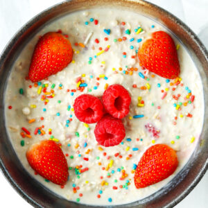 Bowl with overnight oats, rainbow sprinkles, strawberries and raspberries.