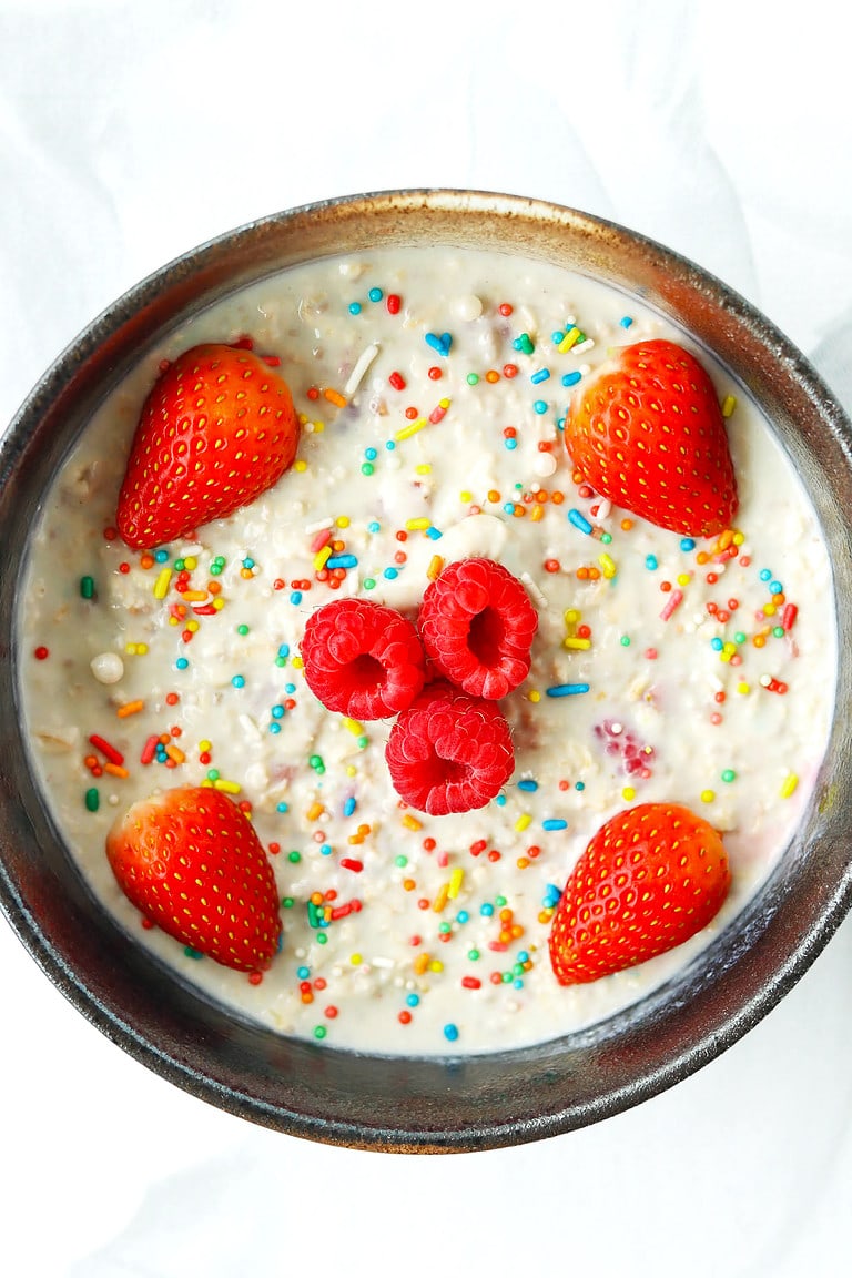 Bowl with overnight oats, rainbow sprinkles, strawberries and raspberries.