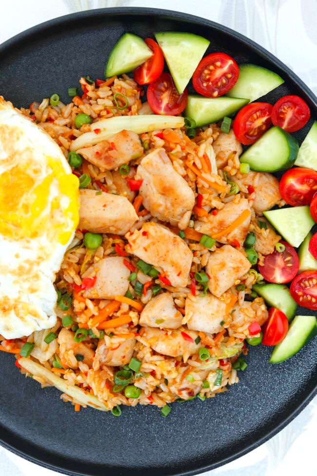 Closeup of chicken nasi goreng topped with a fried egg on a black plate.