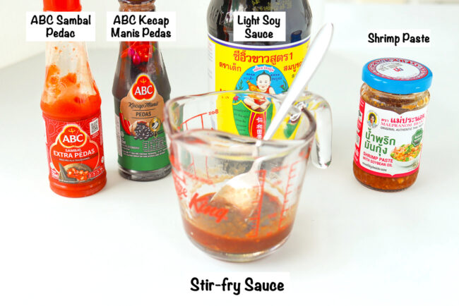 Labeled sauce bottles and nasi goreng sauce in a measuring cup with a spoon.
