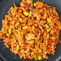 Closeup top view of gochujang cauliflower fried rice on a plate. Text overlay "Korean Cauliflower Fried Rice" and "thatspicychick.com".