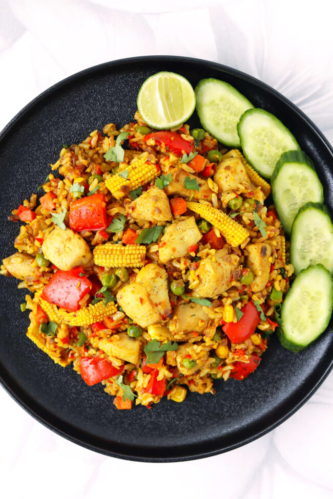 Top view of yellow curry fried rice with chicken, cucumber and lime on a plate.
