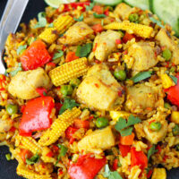 Closeup front view of fried rice on a plate with utensils. Text overlay "Thai Yellow Curry Fried Rice with Chicken" and "thatspicychick.com".