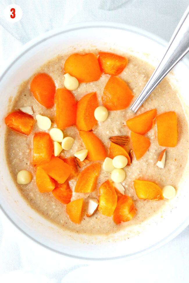 Sliced apricots, white chocolate chips and chopped almonds on batter in a bowl.