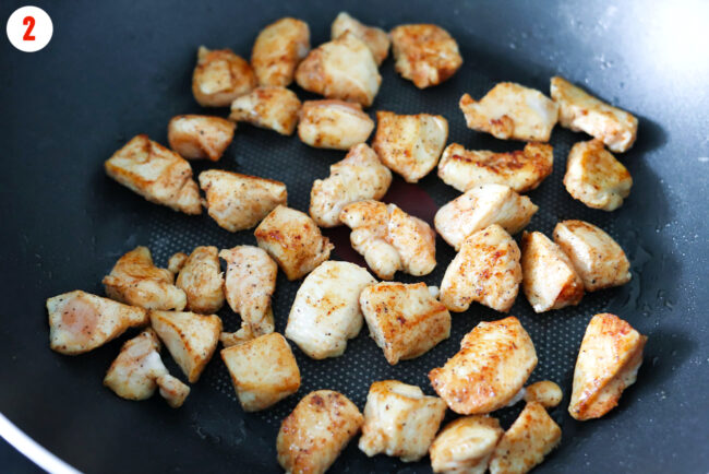 Seared seasoned diced chicken breast pieces in a wok.