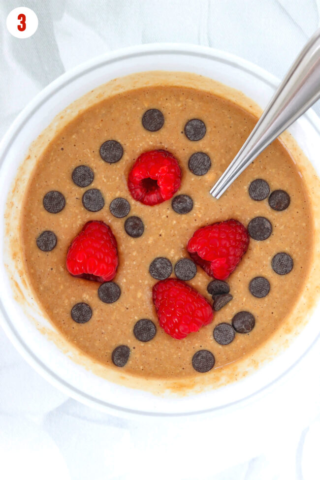 Batter with raspberries and dark chocolate chips in a bowl with a spoon.