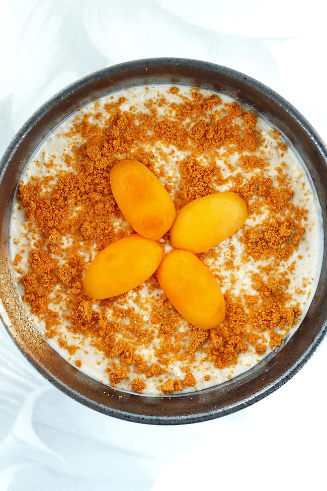 Bowl with snickerdoodle protein overnight oats topped with crushed Biscoff cookie and a sliced apricot.