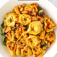 Tortellini and ground chicken stir-fry on a plate. Text overlay "Thai Basil Chicken Tortellini" and "thatspicychick.com"