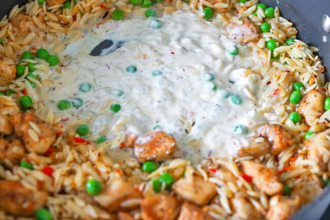 Creamy cheese sauce in pan with pasta, peas and chicken.