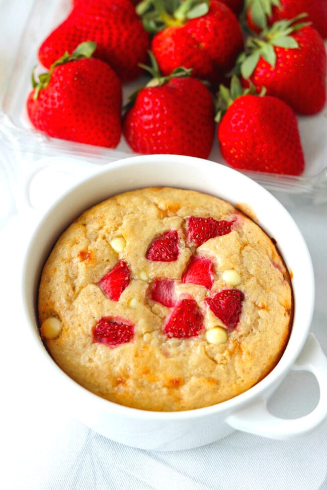 Front view of strawberry cheesecake baked oats in a ramekin and strawberries behind.