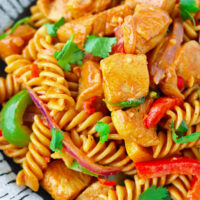 Closeup front view of chicken pasta with peppers, onion and cilantro on a plate. Text overlay "One Pot Chicken Fajita Pasta" and "thatspicychick.com".