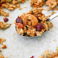 Front view of granola on a spoon on a tray with granola clusters. Text overlay "Maple Tahini Granola", "Easy | Vegan | GF | DF" and "thatspicychick.com".
