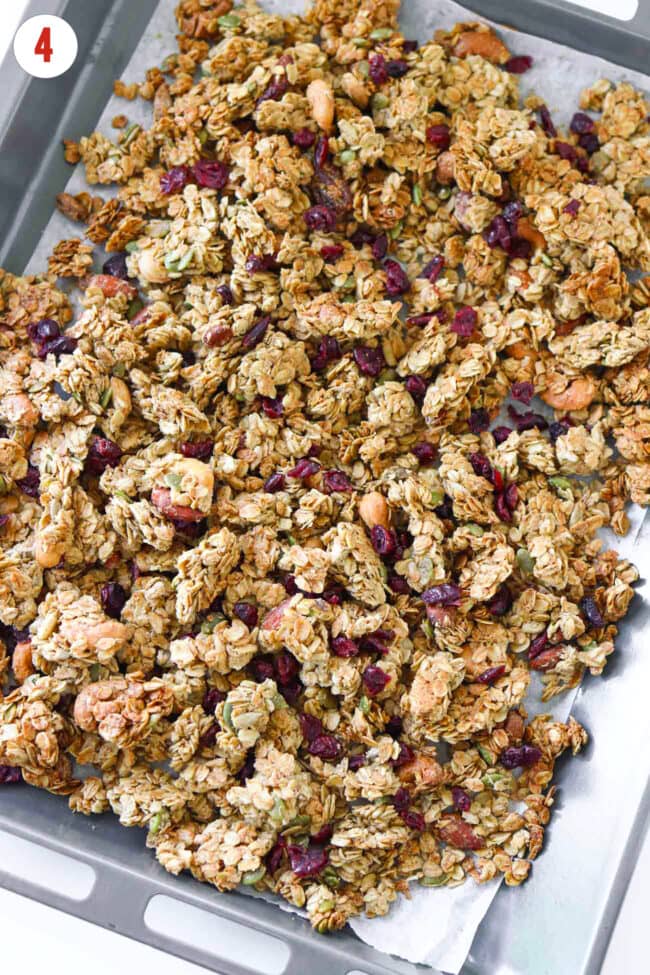 Stirred dried cranberries through maple tahini granola clusters on a baking tray.