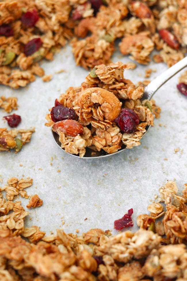 Maple tahini granola on a large spoon on a tray with granola clusters.