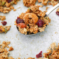 Granola on a spoon on a tray with granola clusters. Closeup front and top view of granola on a large spoon on a tray with granola. Text overlay "Maple Tahini Granola", "Easy | Vegan | GF | DF" and "thatspicychick.com".