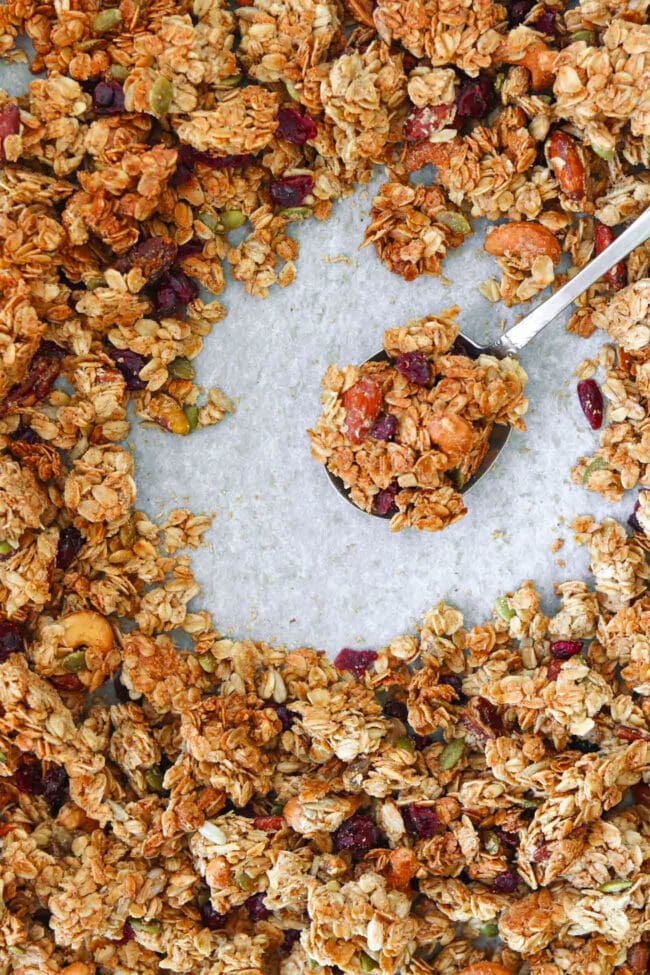 Top view of maple tahini granola on a spoon on a tray with granola clusters.