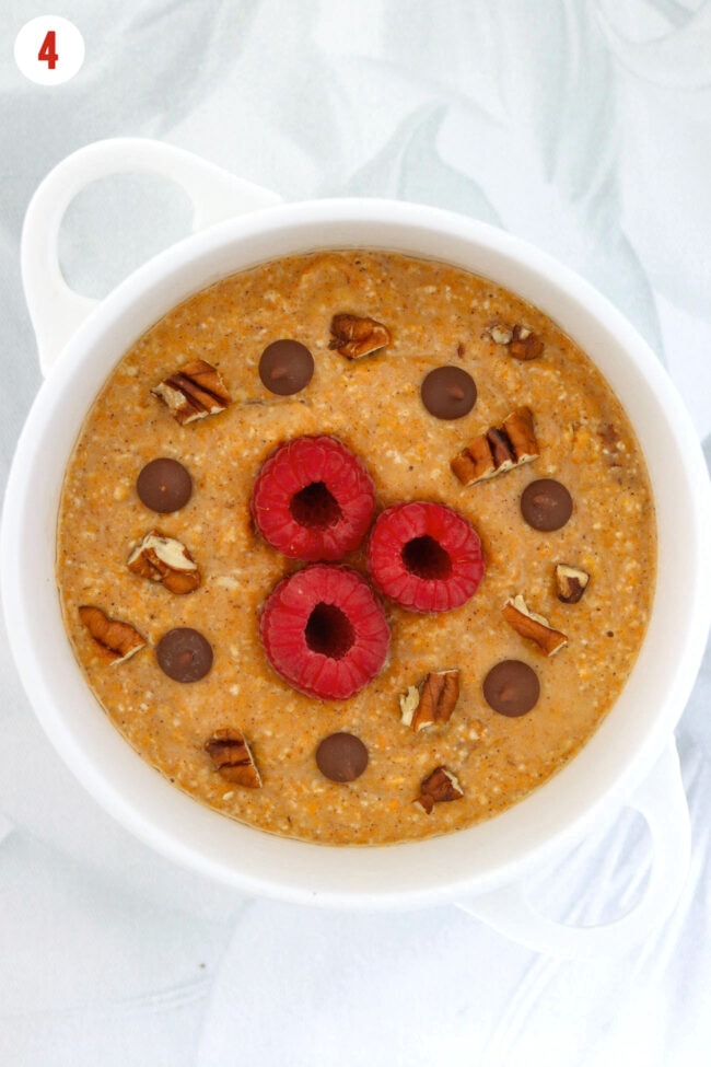 Batter for pumpkin baked oats in a ramekin topped with pecans, raspberries and chocolate chips.