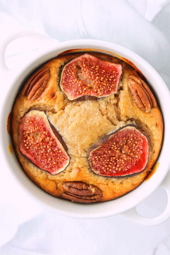 Almond butter baked oatmeal topped with fig slices and pecans in ramekin.