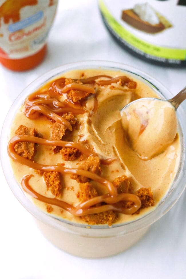 Spoon in pint of pumpkin pie ice cream topped with crushed Biscoff cookie and caramel syrup.