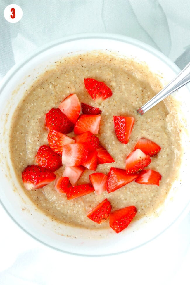 Baked oats batter in a bowl with a spoon topped with chopped strawberries.