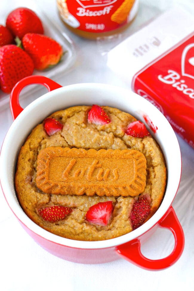 Front view of Biscoff baked oats in a ramekin and strawberries, biscoff jar and cookies behind.