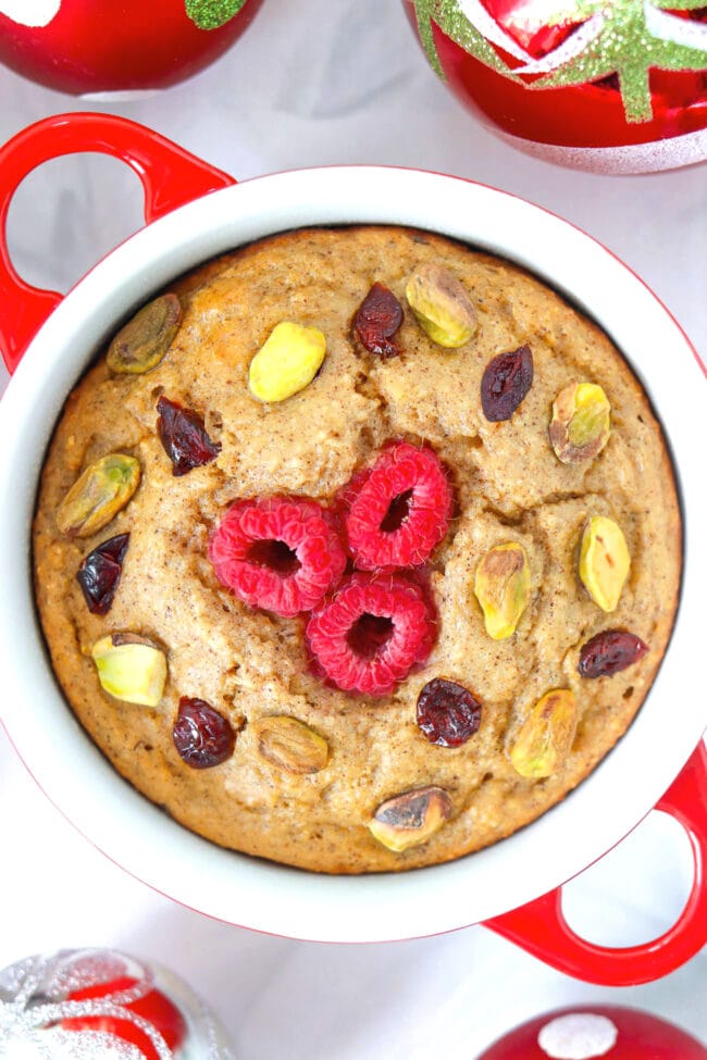 Closeup top view of Cranberry Pistachio Baked Oats in a red ramekin surrounded by Christmas baubles.