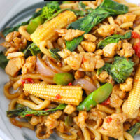 Front view of plate with Thai spicy noodles stir-fry. Text overlay "Pad Kee Mao Udon", "Thai Drunken Udon Noodles" and "thatspicychick.com"