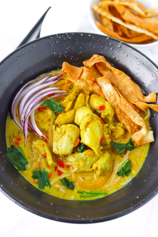Chicken khao soi in a bowl with air-fried wonton strips on a plate behind.