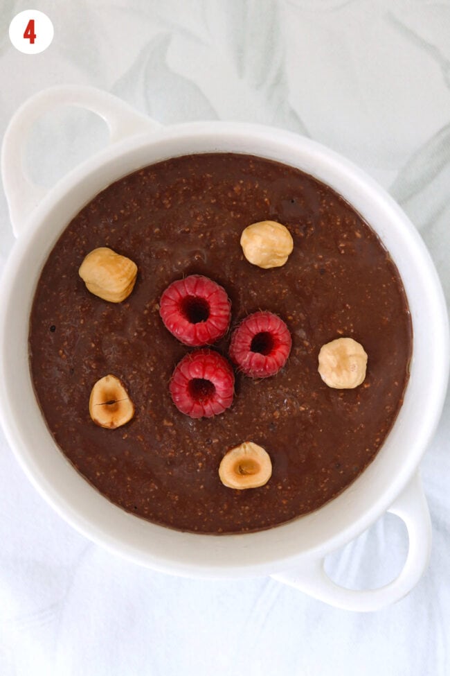 Chocolate baked oats batter with hazelnuts and raspberries in a ramekin.