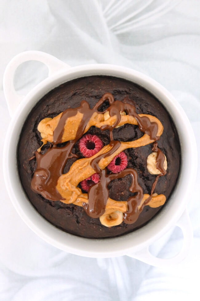 Chocolate hazelnut baked oats topped with peanut butter and chocolate spread in a white ramekin.