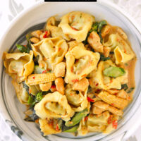 Plate with Thai tortellini dish with veggies and chicken. Text overlay "Thai Green Curry Chicken Tortellini" and "thatspicychick.com".