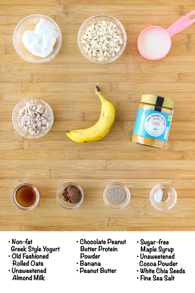 Labeled ingredients for chocolate peanut butter banana overnight oats on a wooden board.