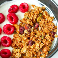 Front view of bowl with granola, raspberries on yogurt. Text overlay "Peanut Butter Granola", "High Protein | Gluten-free" and "thatspicychick.com".