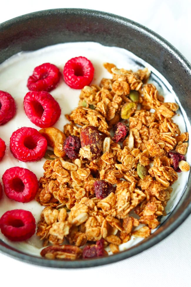 Front view closeup of bowl with granola, raspberries on Greek yogurt.