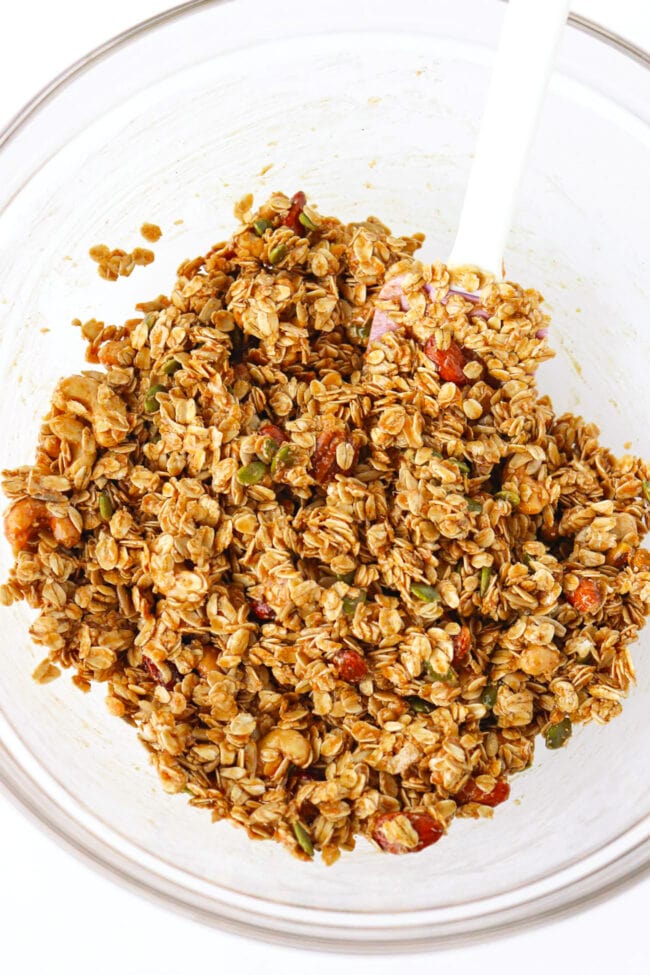 Combined dry and wet ingredients for peanut butter granola in a bowl with a silicone spatula.